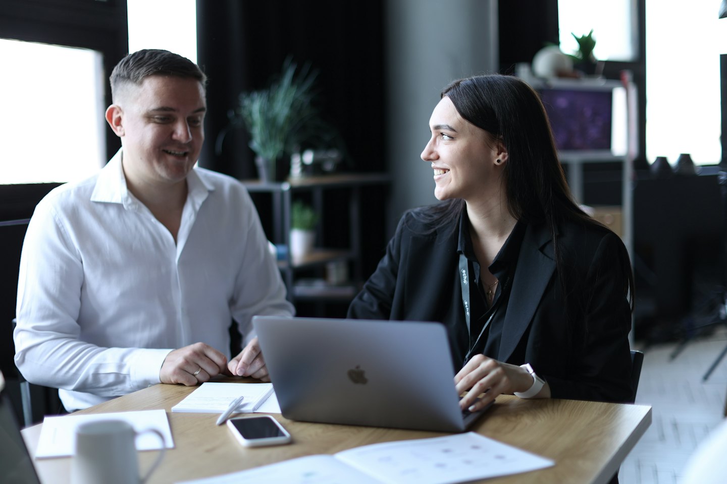 Two professionals collaborating over a laptop at a wooden table.